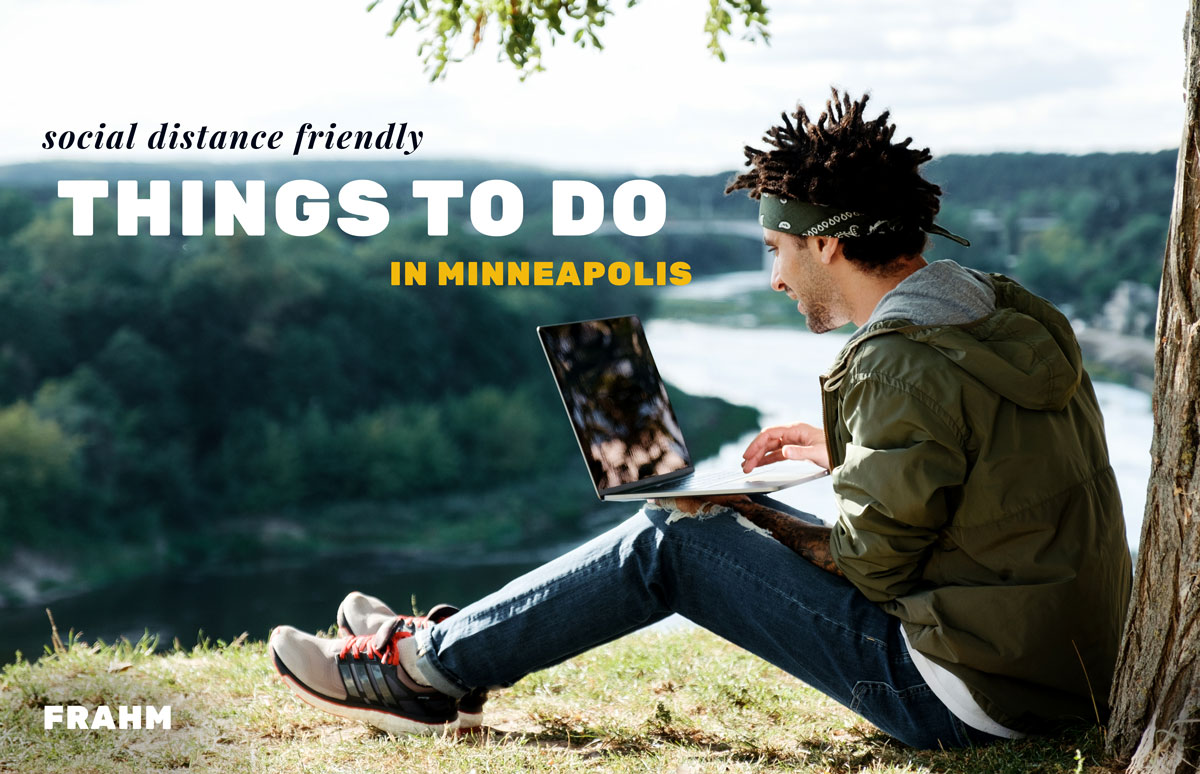 Man sitting above the Mississippi River in Minneapolis looking at a laptop and smiling